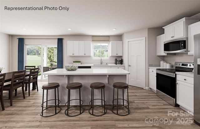 kitchen with white cabinetry, appliances with stainless steel finishes, a center island, and light wood-type flooring