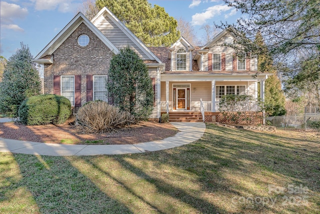 traditional home featuring a porch, a front yard, fence, and brick siding