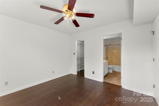 unfurnished bedroom featuring dark wood-type flooring, ceiling fan, connected bathroom, a spacious closet, and a closet