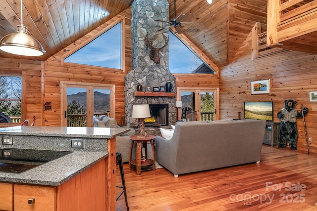 living room featuring wood ceiling, a stone fireplace, and wood walls