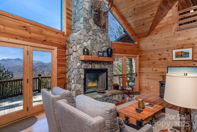 living room featuring light hardwood / wood-style flooring, a fireplace, a mountain view, beamed ceiling, and wood walls