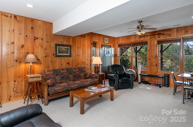 carpeted living room with ceiling fan and wood walls