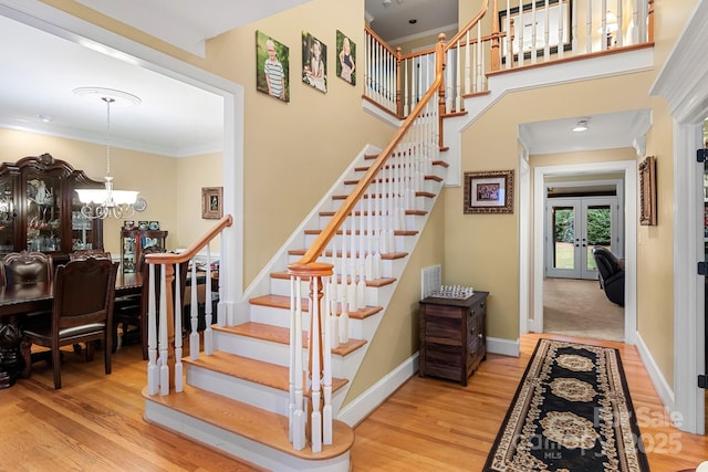 stairway featuring crown molding, an inviting chandelier, hardwood / wood-style floors, a high ceiling, and french doors