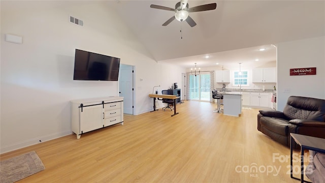 living room with high vaulted ceiling, ceiling fan with notable chandelier, and light hardwood / wood-style floors