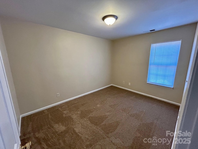 spare room with baseboards, visible vents, and dark colored carpet