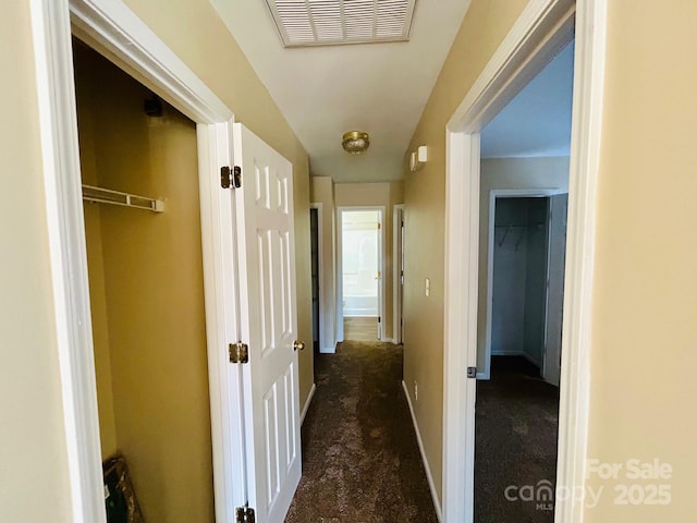 hallway with baseboards, visible vents, and dark colored carpet