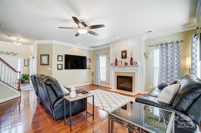 living area featuring crown molding, a ceiling fan, a fireplace with flush hearth, wood finished floors, and stairs