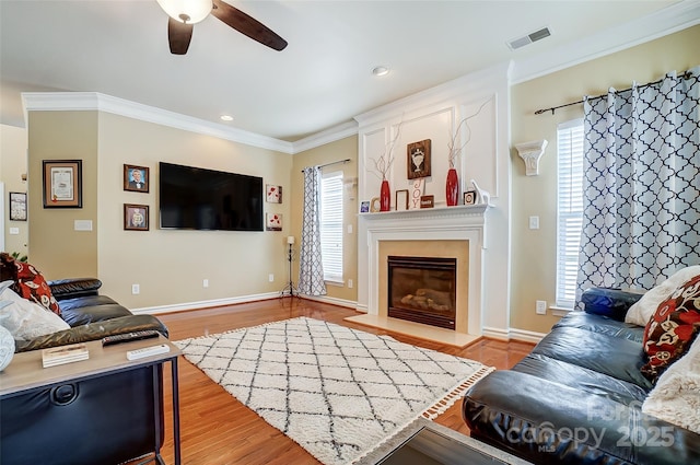 living room with visible vents, light wood-style flooring, ornamental molding, a ceiling fan, and baseboards