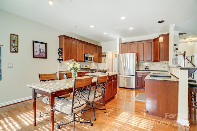 kitchen featuring light wood-type flooring, light stone countertops, stainless steel appliances, and a sink