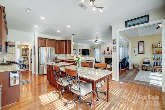 dining room featuring ceiling fan with notable chandelier, a fireplace, visible vents, and light wood-style floors