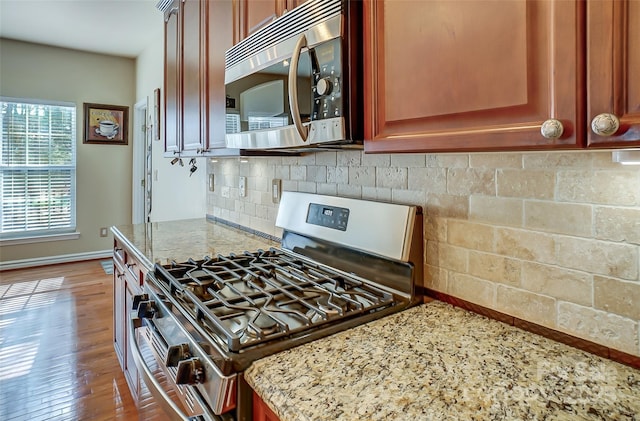 kitchen featuring light stone countertops, dark wood-type flooring, baseboards, appliances with stainless steel finishes, and decorative backsplash