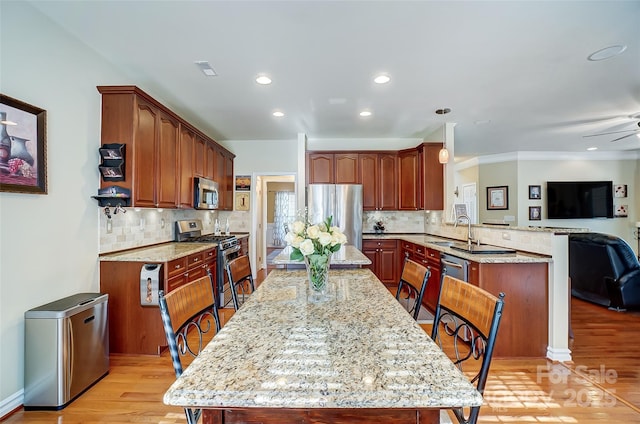 kitchen with appliances with stainless steel finishes, open floor plan, a peninsula, light stone countertops, and light wood-type flooring