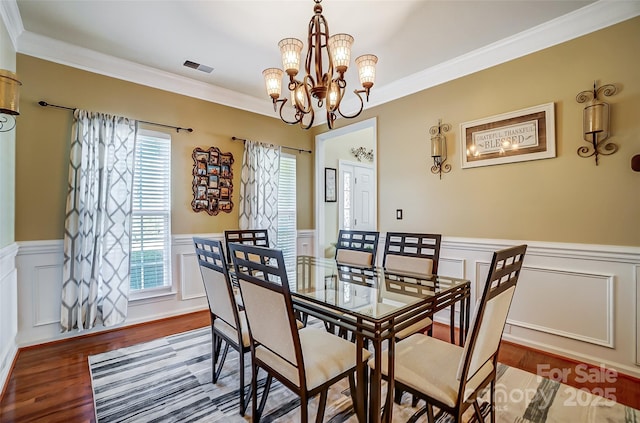 dining space featuring ornamental molding, wainscoting, a notable chandelier, and wood finished floors