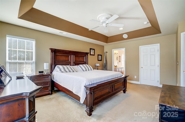 bedroom with ensuite bathroom, light carpet, visible vents, baseboards, and a tray ceiling