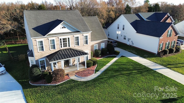 view of front of home with a shingled roof, a front lawn, a porch, and brick siding