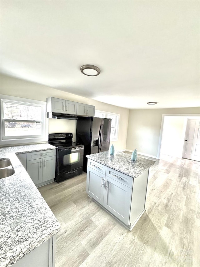 kitchen with light wood-style flooring, a kitchen island, black electric range oven, light stone countertops, and gray cabinets