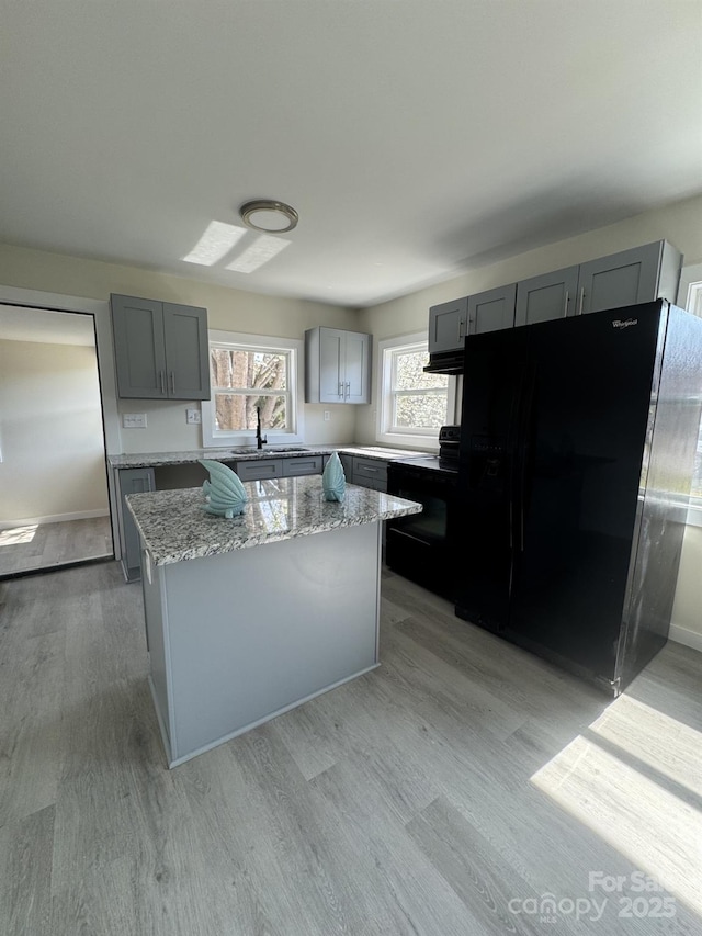 kitchen featuring black appliances, gray cabinets, a sink, a kitchen island, and light wood finished floors