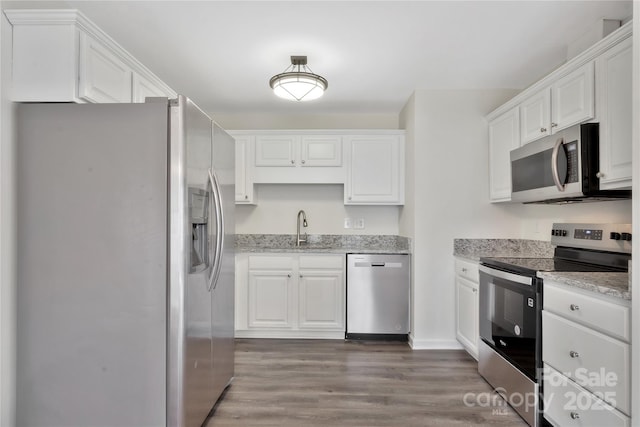 kitchen with light stone countertops, appliances with stainless steel finishes, dark hardwood / wood-style floors, and white cabinets