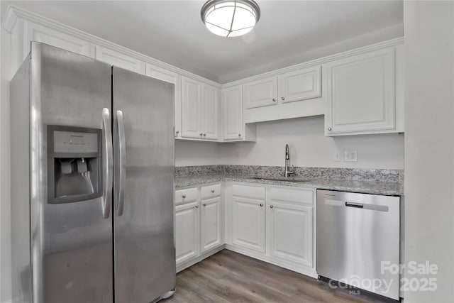 kitchen with appliances with stainless steel finishes, dark hardwood / wood-style floors, white cabinetry, sink, and light stone counters