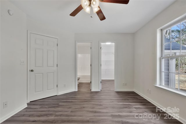 unfurnished bedroom featuring ensuite bathroom, dark hardwood / wood-style floors, a walk in closet, ceiling fan, and a closet