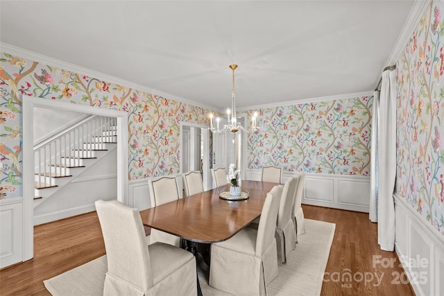 dining area with dark wood-style flooring, a notable chandelier, stairway, wainscoting, and wallpapered walls