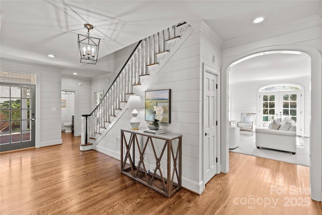 foyer featuring arched walkways, french doors, ornamental molding, wood finished floors, and stairs