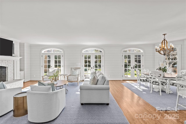 living room featuring french doors, a brick fireplace, wood finished floors, and an inviting chandelier