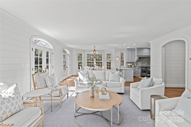 living area with ornamental molding, french doors, a chandelier, and light wood-style flooring