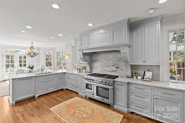 kitchen featuring range with two ovens, tasteful backsplash, a sink, light stone countertops, and light wood-type flooring