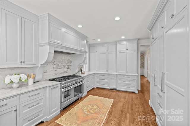 kitchen featuring decorative backsplash, white cabinetry, range with two ovens, and light stone counters