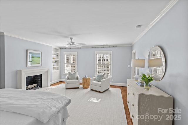 bedroom with a fireplace, a ceiling fan, baseboards, light wood-style floors, and crown molding