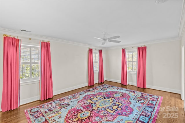 spare room featuring ceiling fan, ornamental molding, wood finished floors, and visible vents