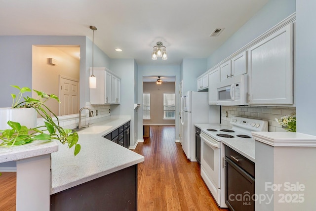 kitchen featuring decorative light fixtures, sink, light hardwood / wood-style floors, kitchen peninsula, and white appliances