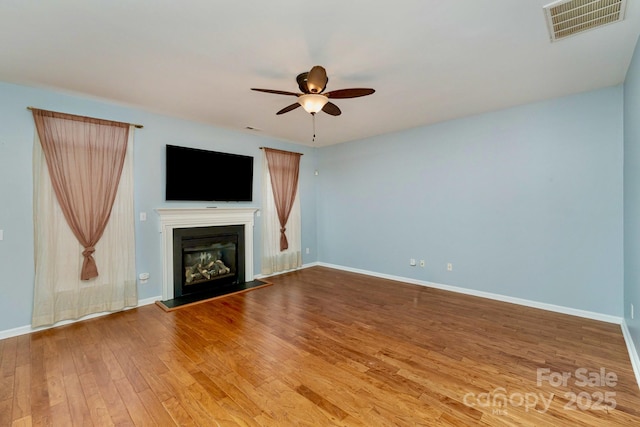 unfurnished living room featuring ceiling fan, visible vents, baseboards, wood-type flooring, and a glass covered fireplace