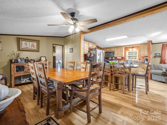 dining area with a ceiling fan, vaulted ceiling, a textured ceiling, crown molding, and light wood-style floors