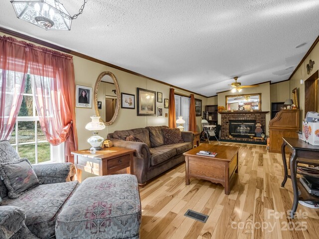 living area featuring ceiling fan, visible vents, a brick fireplace, light wood finished floors, and crown molding