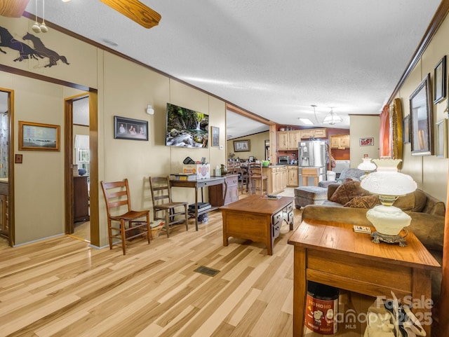 living area with visible vents, lofted ceiling, a textured ceiling, crown molding, and light wood-style floors