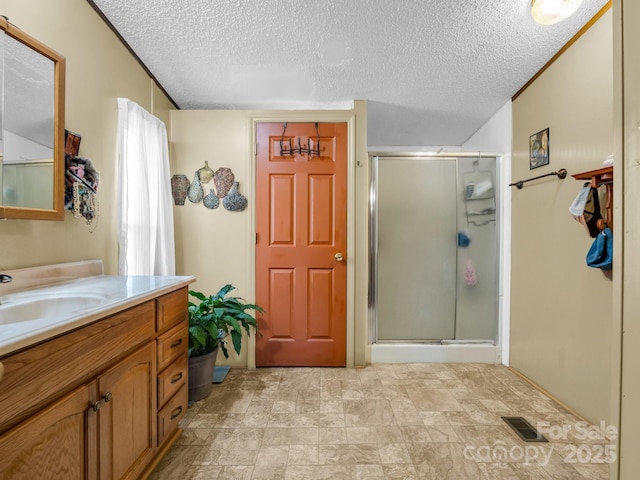 full bathroom featuring a textured ceiling, vanity, a shower stall, and visible vents