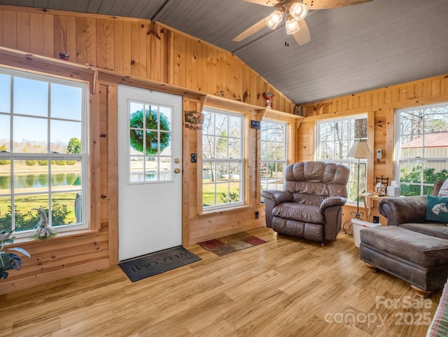 living area with lofted ceiling, a wealth of natural light, light wood-style flooring, and wooden walls