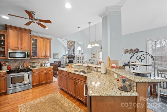 kitchen featuring brown cabinetry, a kitchen bar, a sink, ceiling fan with notable chandelier, and stainless steel appliances