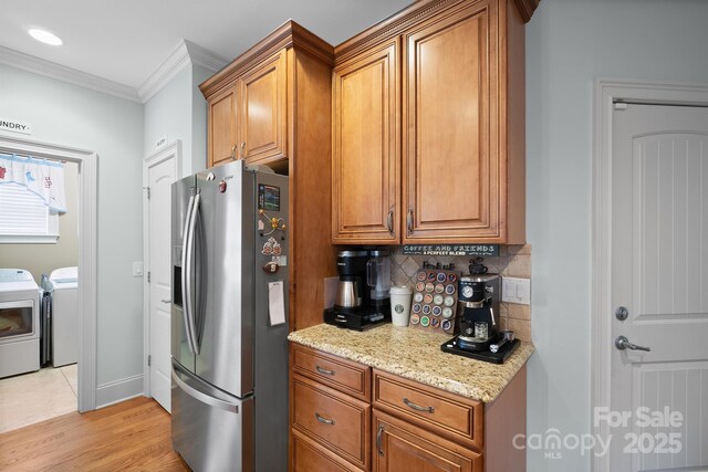 kitchen featuring stainless steel fridge, crown molding, washing machine and dryer, and brown cabinets