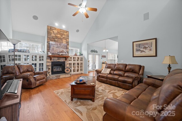 living room with light wood finished floors, ceiling fan, high vaulted ceiling, and a fireplace