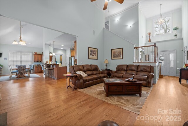 living room featuring light wood-type flooring, a ceiling fan, a towering ceiling, and crown molding