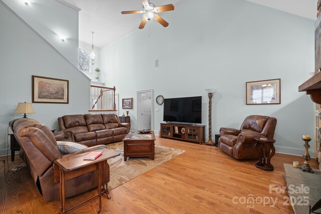 living room with a ceiling fan, a towering ceiling, baseboards, light wood-style floors, and stairs