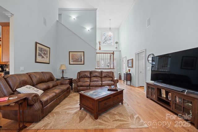 living room with visible vents, ornamental molding, light wood-style flooring, and a towering ceiling