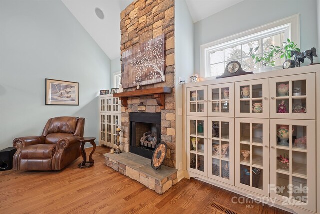 living area with a stone fireplace, wood finished floors, vaulted ceiling, and visible vents