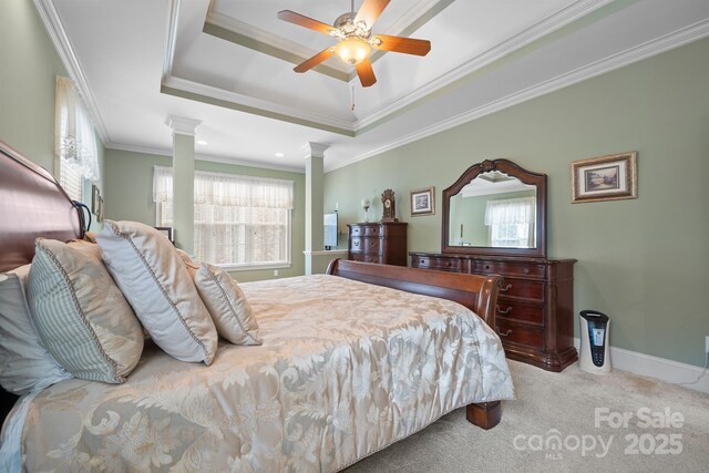 carpeted bedroom with crown molding, decorative columns, baseboards, a raised ceiling, and a ceiling fan
