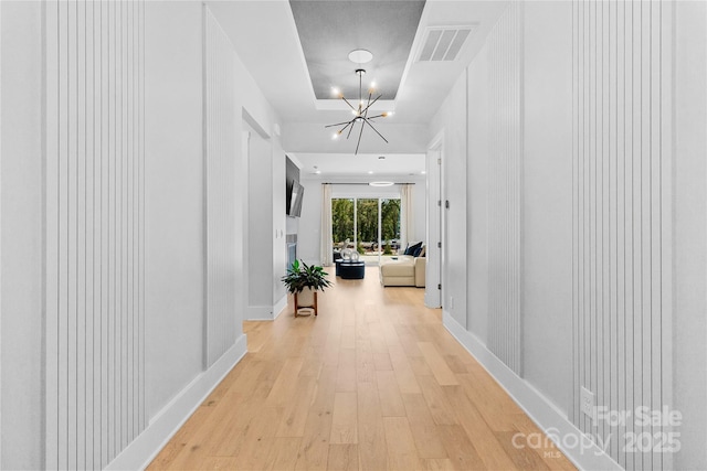 hallway with light wood-style flooring, visible vents, a chandelier, and baseboards