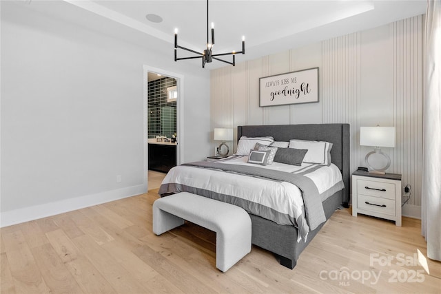 bedroom featuring light wood finished floors, ensuite bath, baseboards, and an inviting chandelier