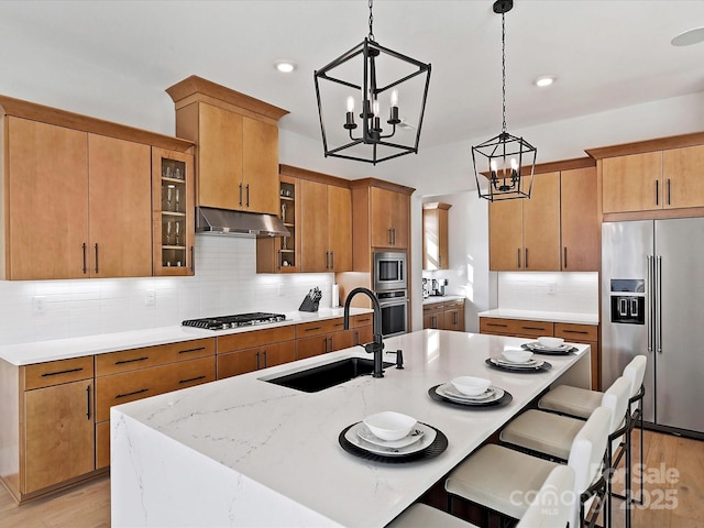 kitchen with under cabinet range hood, stainless steel appliances, a sink, backsplash, and pendant lighting